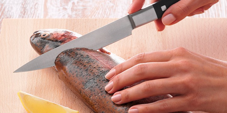 A chef expertly fillets a fish on a wooden board with a Fissler precision knife; next to it is Fissler cookware and a lemon wedge.