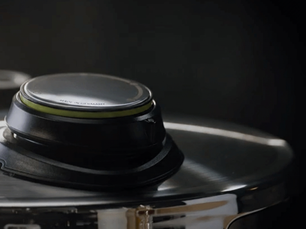 Close-up of a Fissler stainless steel pot lid, featuring a distinctive black and green ergonomic handle, masterfully engineered for durability and comfort. The lid’s polished surface reflects our German heritage of precision and timeless design, set against an elegant dark background.