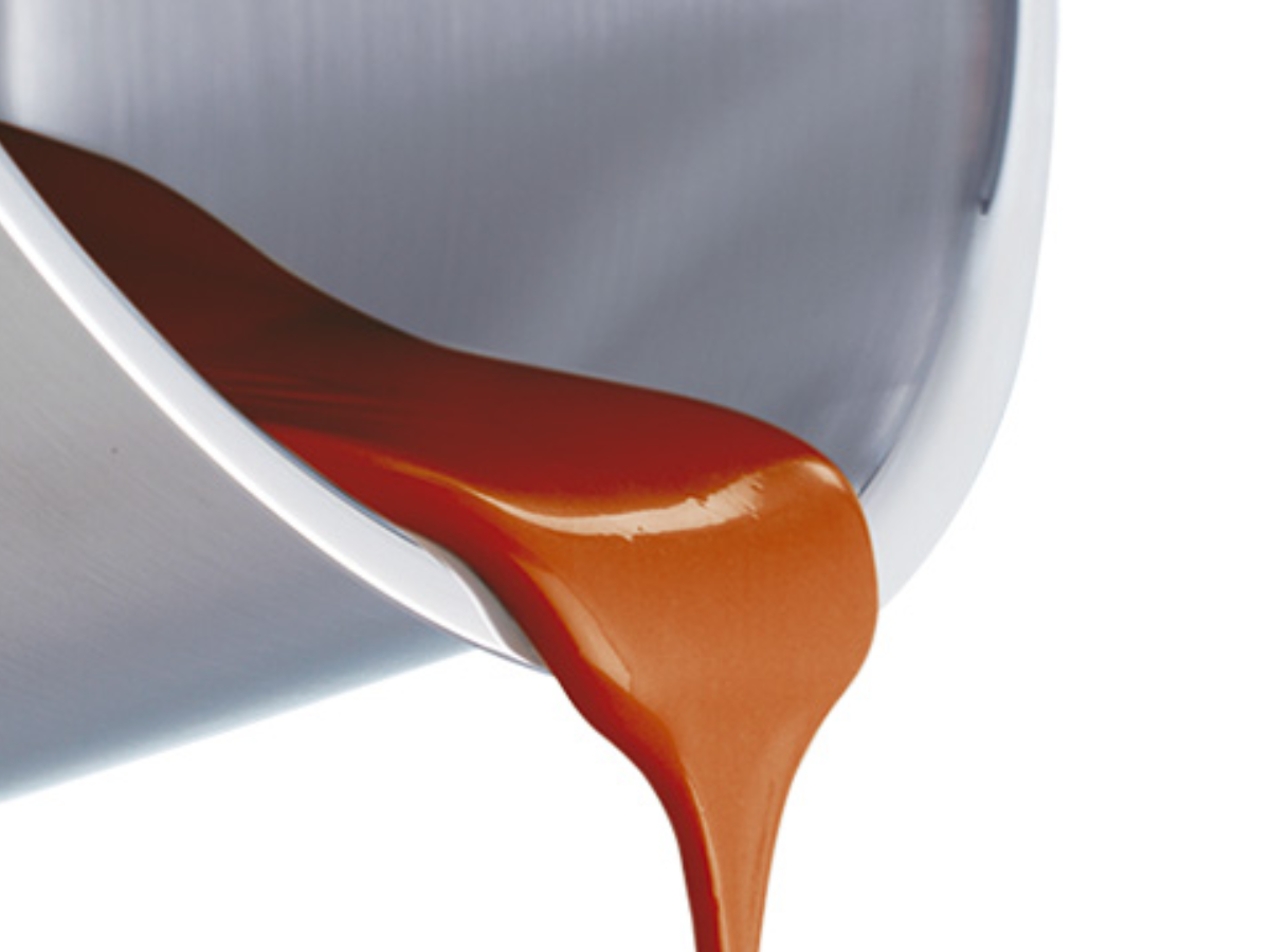 Caramel sauce gently flowing down the side of a high-quality Fissler stainless steel bowl reflects precise German craftsmanship.