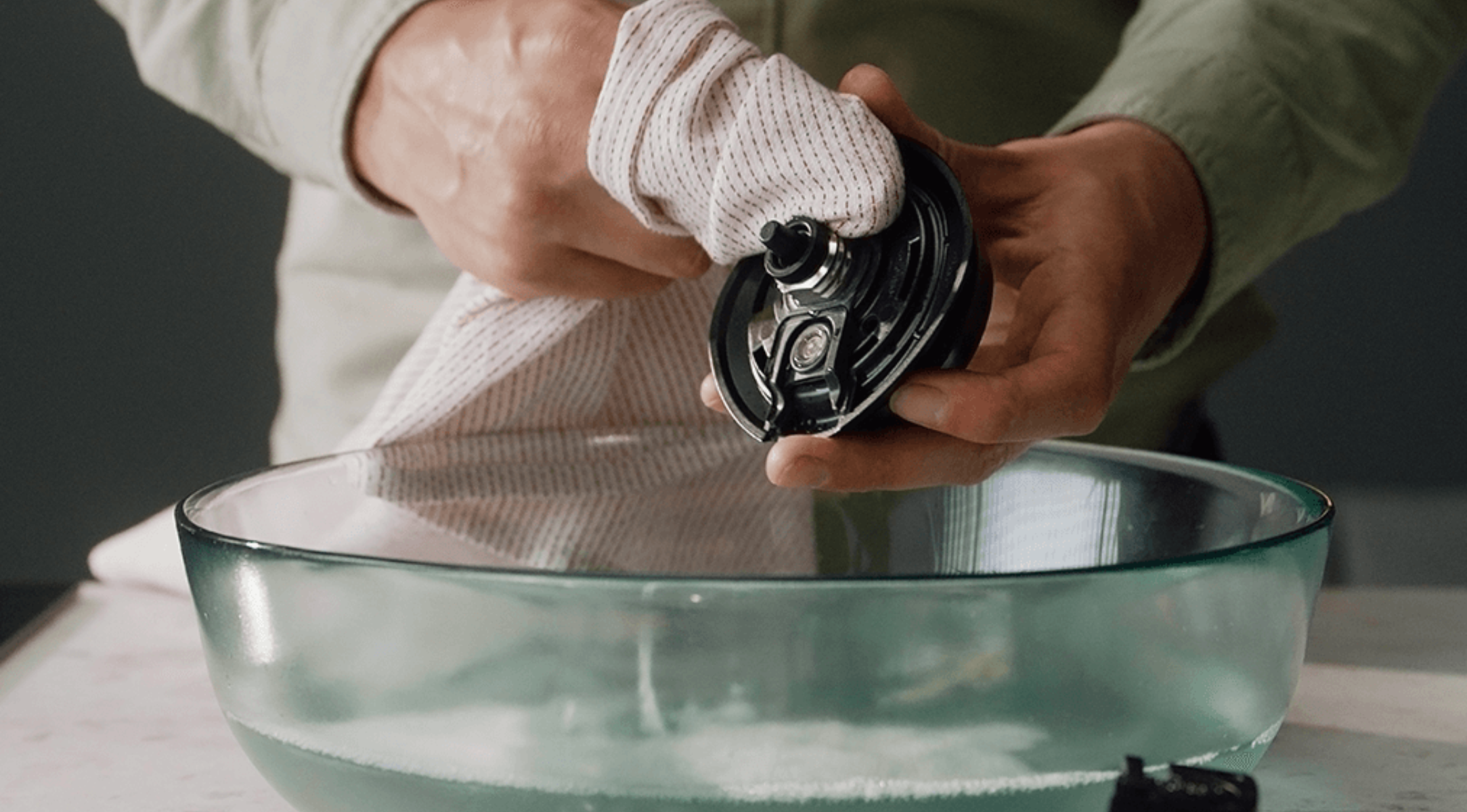 Eine Person trocknet sorgfältig ein Fissler-Geräteteil mit einem Handtuch über einer Glasschüssel mit Wasser, was von deutscher Präzision und Qualität zeugt.
