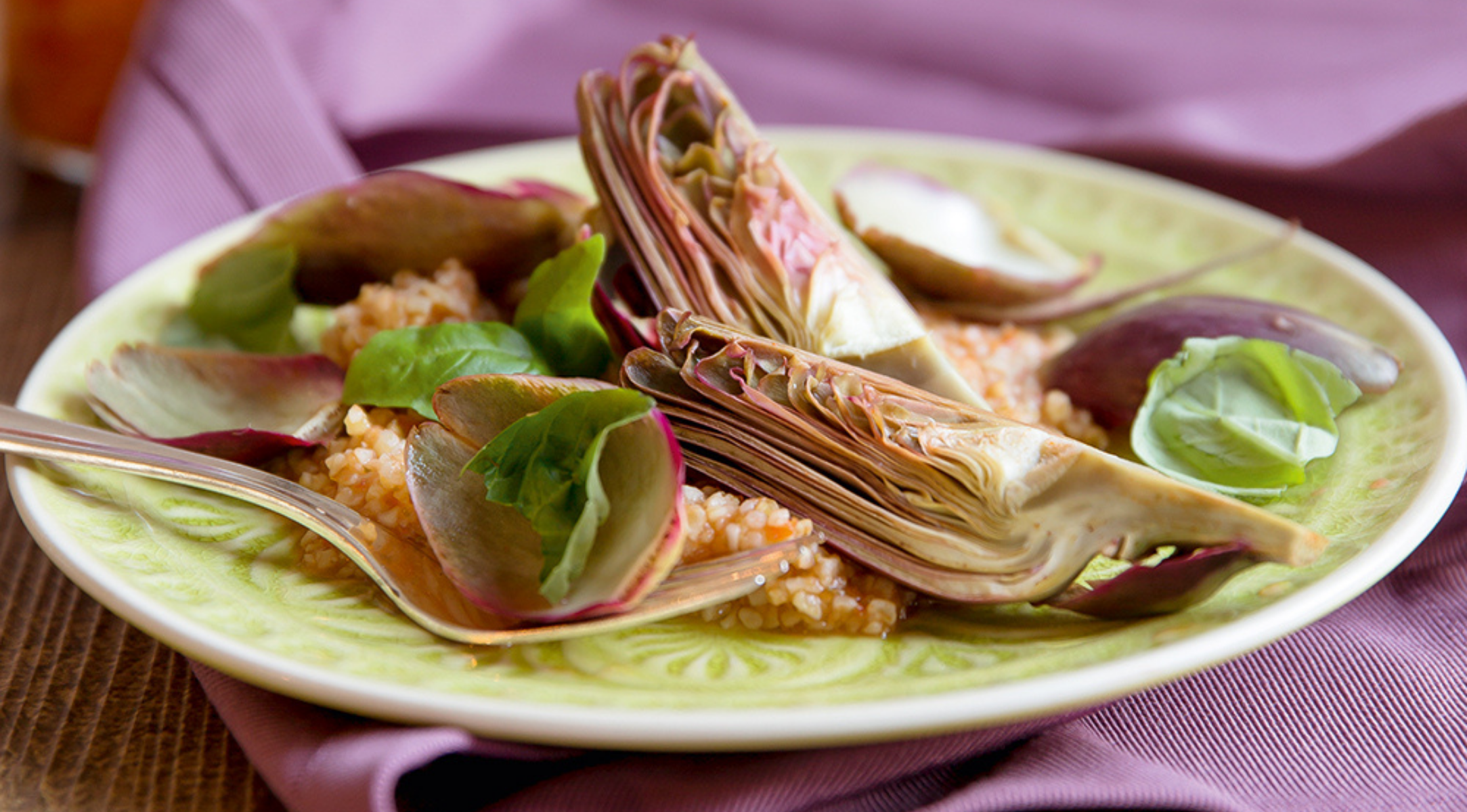 Couscous mit Artischocken und Basilikum wird auf feinem Geschirr neben einer Gabel serviert und zeigt die zeitlose Präzision des Fissler Kochgeschirrs.
