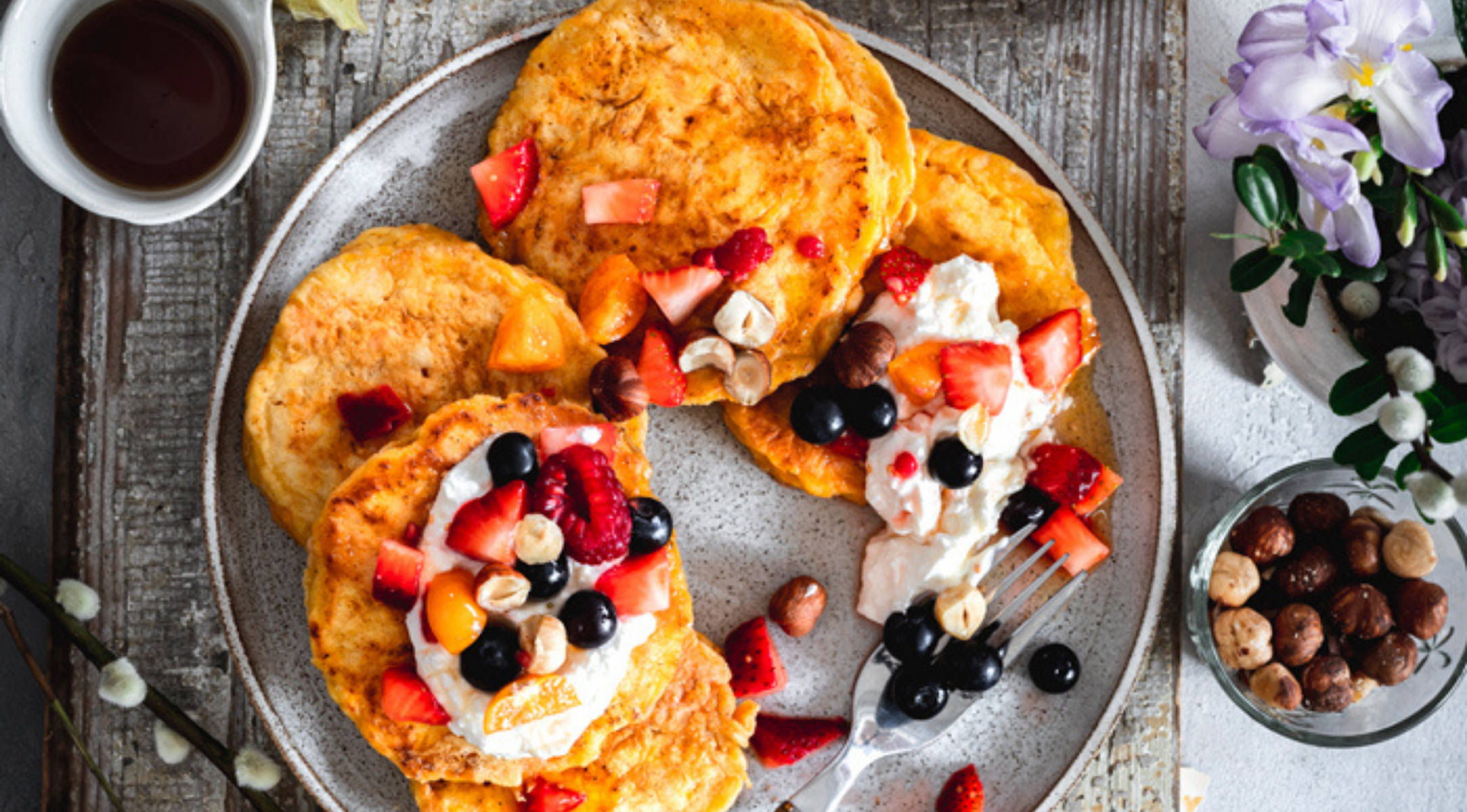 Goldene Pfannkuchen mit Beeren und Sahne, kunstvoll auf rustikalem Geschirr präsentiert - neben dem eleganten Kochgeschirr von Fissler.