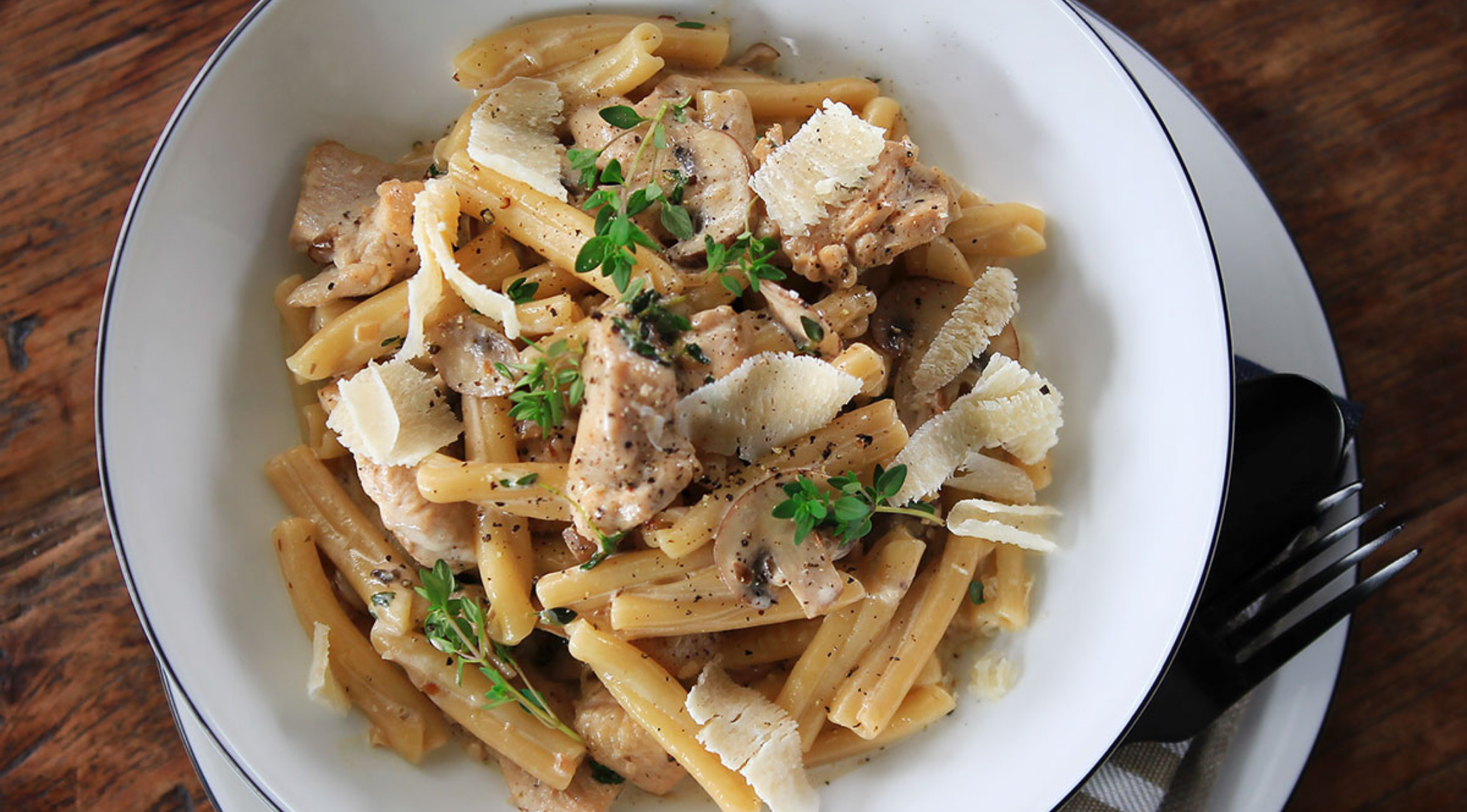 Cremige Hühnerpasta mit Parmesan und Kräutern, schön angerichtet mit Fissler-Besteck auf einem Holztisch, der ein präzises Design zeigt.