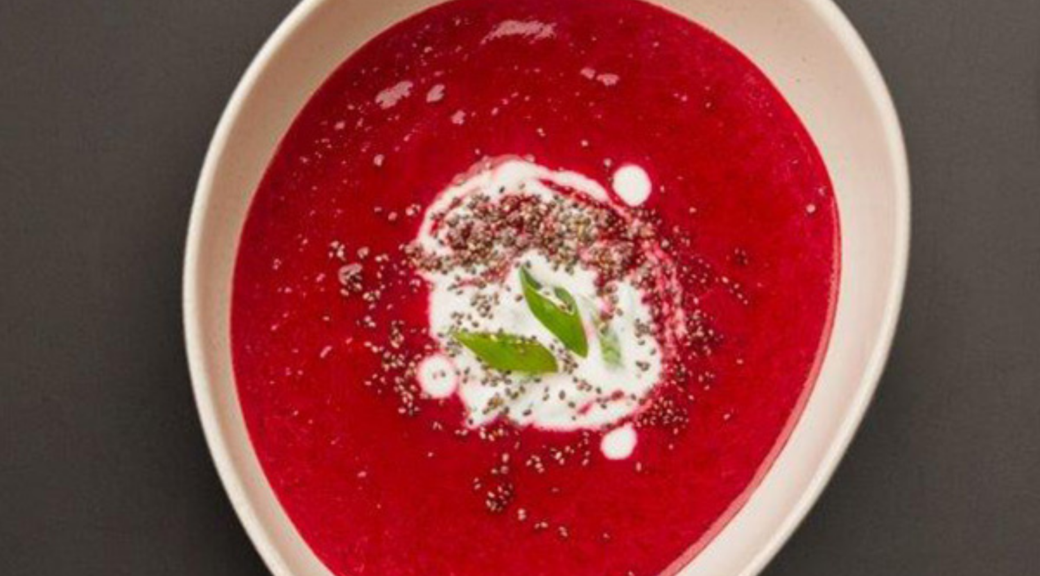 Eine kräftige Rote-Bete-Suppe mit Sahne, Pfeffer und Kräutern in einer weißen Schale - hergestellt mit Fissler Premium-Kochgeschirr auf dunklem Hintergrund.