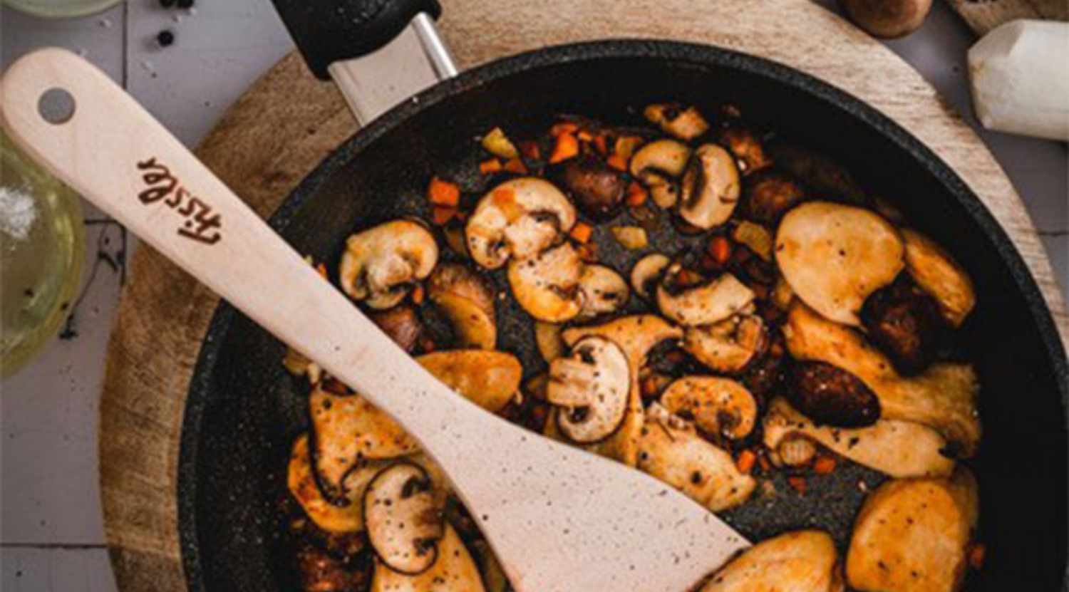 Fissler-Pfanne mit Champignons und Gemüse beim Anbraten, dazu ein Fissler-Holzspatel - deutsches Präzisionskochgeschirr.