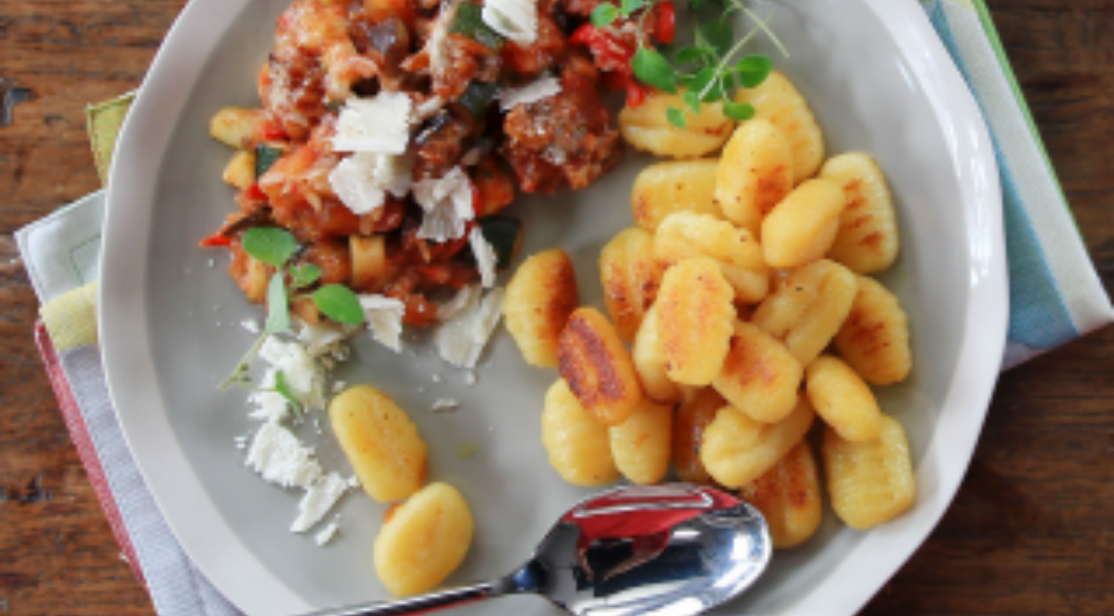 Goldbraune Gnocchi und pikante Fleisch-Gemüse-Sauce, garniert und serviert mit Fissler-Besteck auf eleganten Servietten.