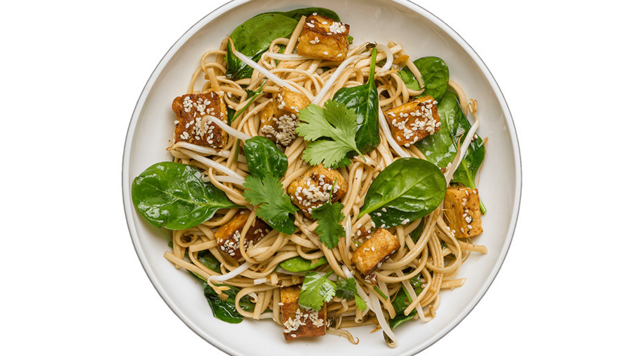 Nudelsalat mit Tofu, Spinat und frischen Kräutern in einer weißen Schüssel, zubereitet mit Präzisionskochgeschirr von Fissler auf einer sauberen Unterlage.