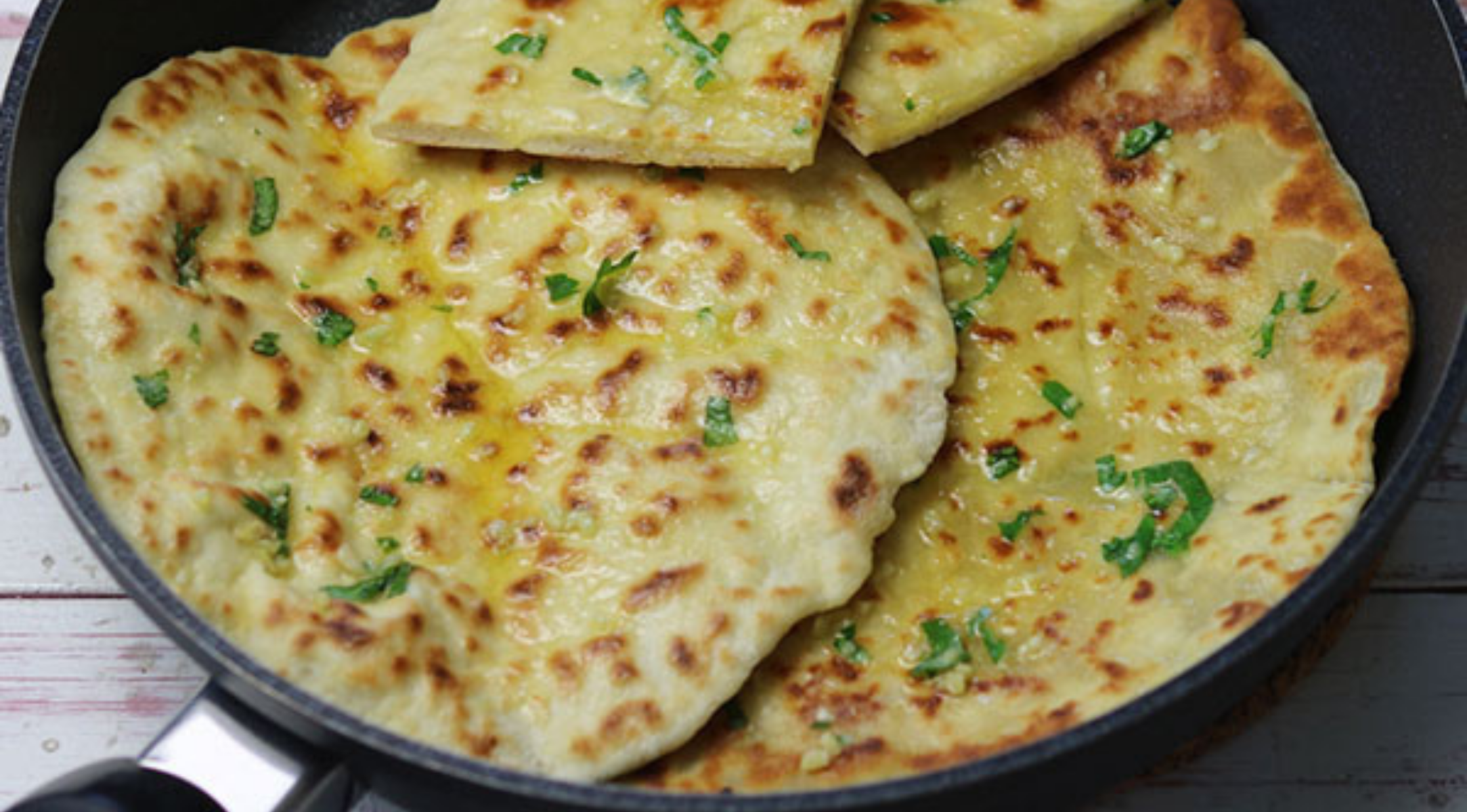Mit Kräutern garnierte, goldene Fladenbrote, die in einer hochwertigen Fissler-Pfanne auf einem hellen Holztisch glänzend präsentiert werden.