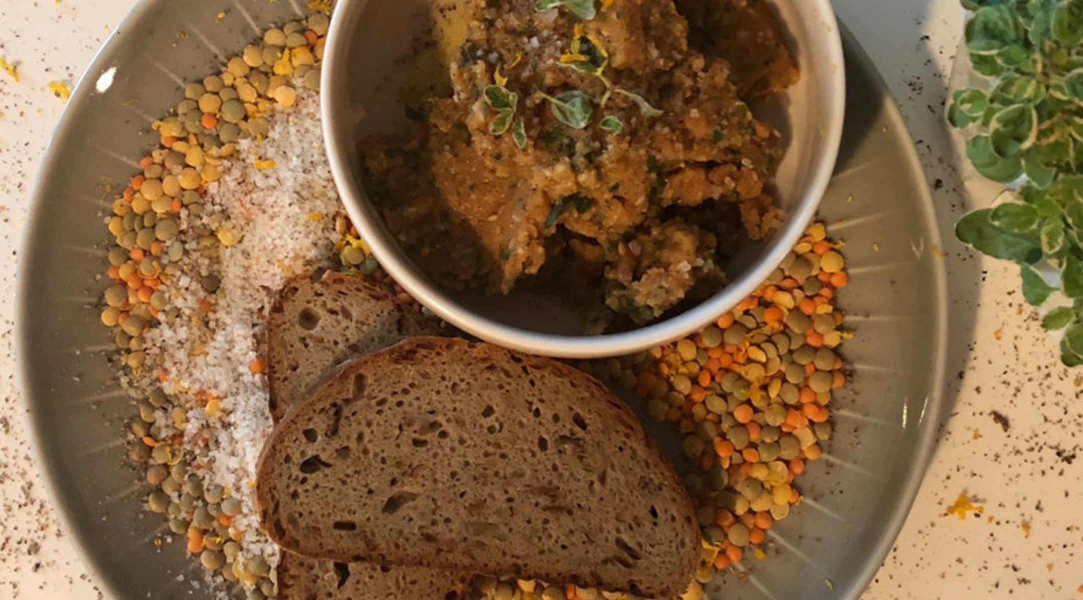 Herzhafter Eintopf mit frischen Kräutern, serviert in einer Fissler-Schale, begleitet von Linsen, Salz, dunklem Brot und kräftigem Grünzeug.