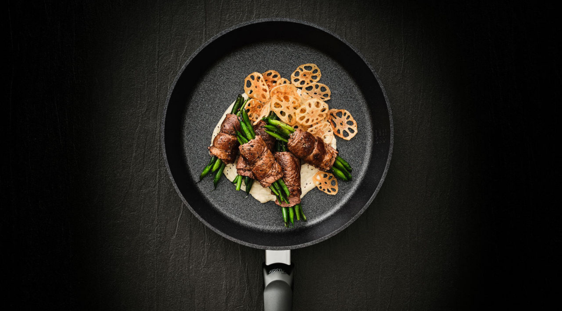 Fissler-Pfanne mit grünen Bohnen in angebratenem Fleisch, Lotuswurzelchips und cremiger Sauce auf dunkler Oberfläche - präzises Kochgeschirr für zeitlose Gerichte.