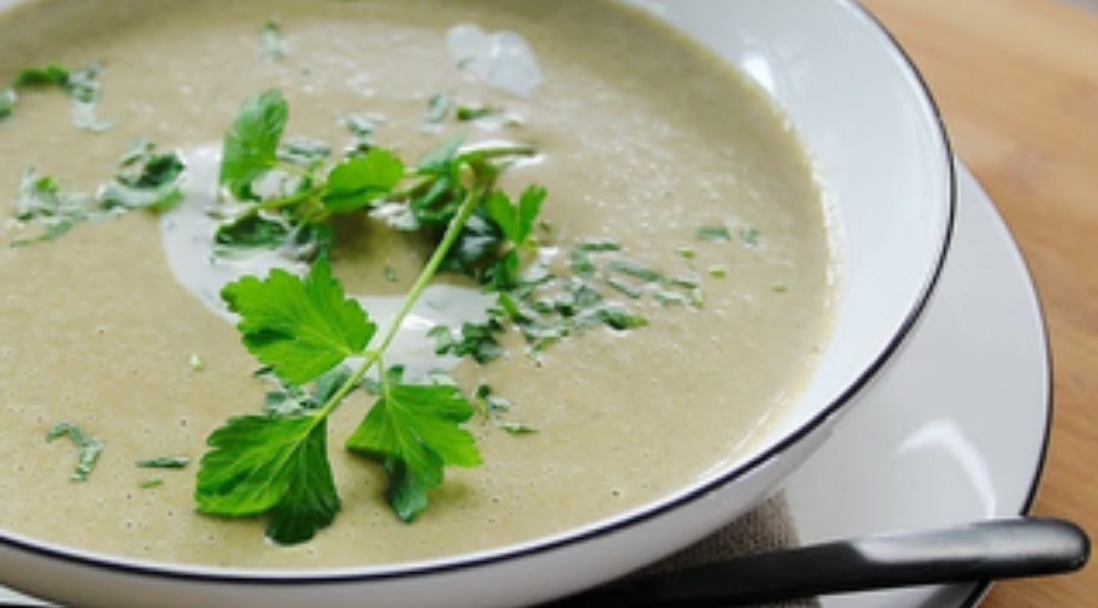 Cremige Suppe mit frischen Kräutern, serviert in einer Fissler-Schale, die deutsches Design und Präzision unterstreicht. Löffel aus Edelstahl daneben.
