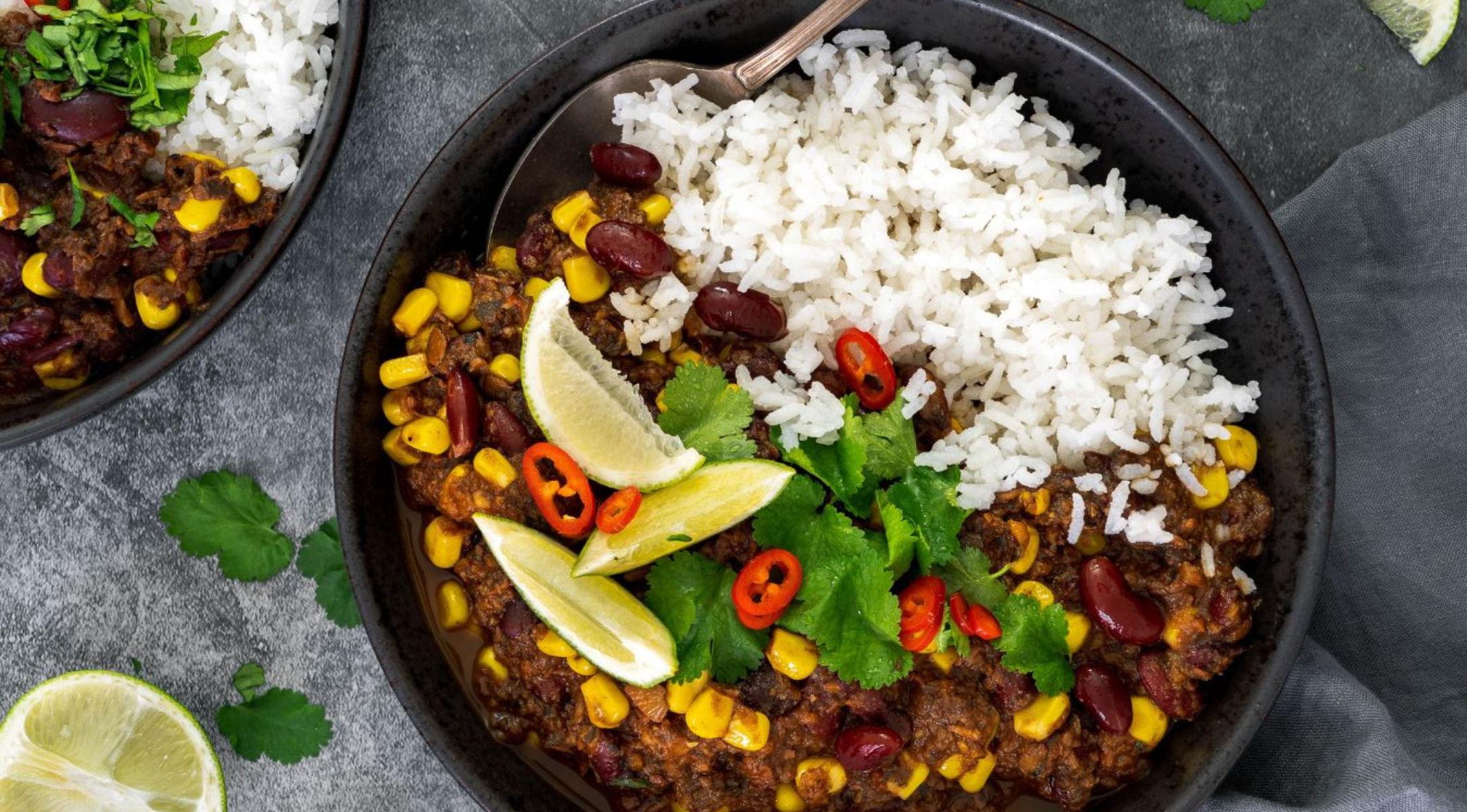 Eine Schüssel mit weißem Reis und Chili con Carne mit frischem Belag, serviert auf einer grauen Oberfläche - zubereitet im hochwertigen Fissler-Kochgeschirr.