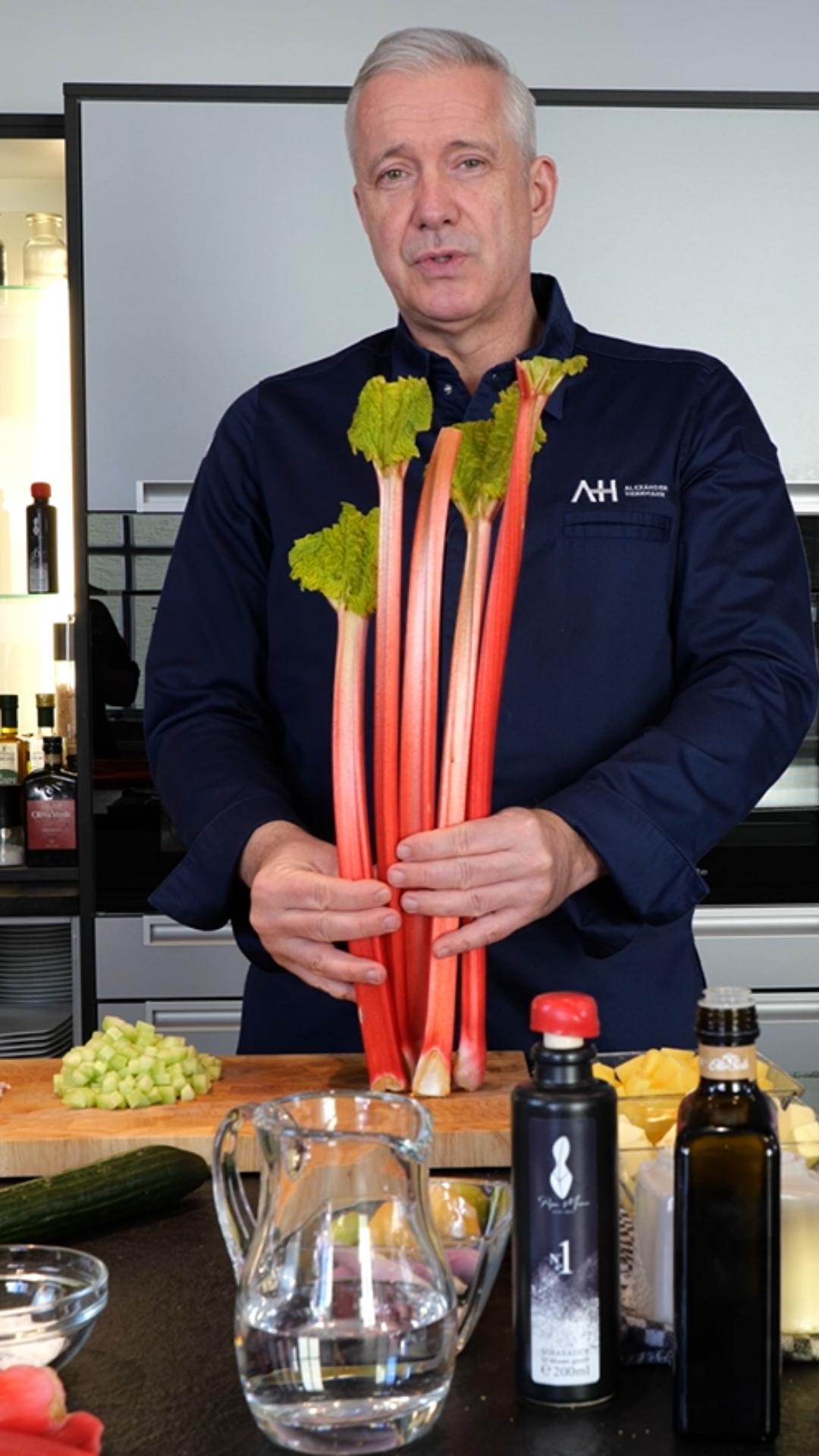 Ein Mann in einer Küche mit Rhabarber, umgeben von gehackten Zutaten und hochwertigem Fissler-Kochgeschirr auf der Theke.