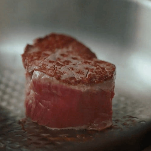 Ein dickes Steak wird in einer Fissler-Pfanne gebraten; seine karamellisierte Kruste steht im Kontrast zu den rosafarbenen, rohen Seiten - Präzisionskochgeschirr bei der Arbeit.