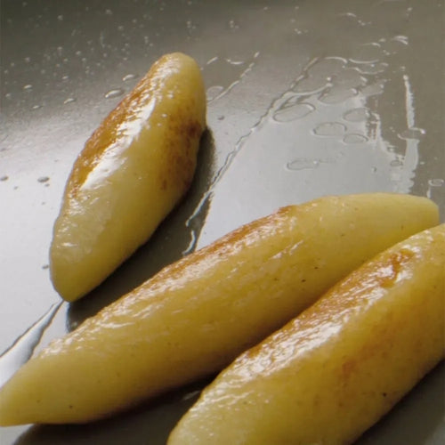 Drei goldbraune Knödel brutzeln in einer Fissler-Pfanne, deren knusprige Kruste die Präzision des deutschen Kochgeschirrs unterstreicht.