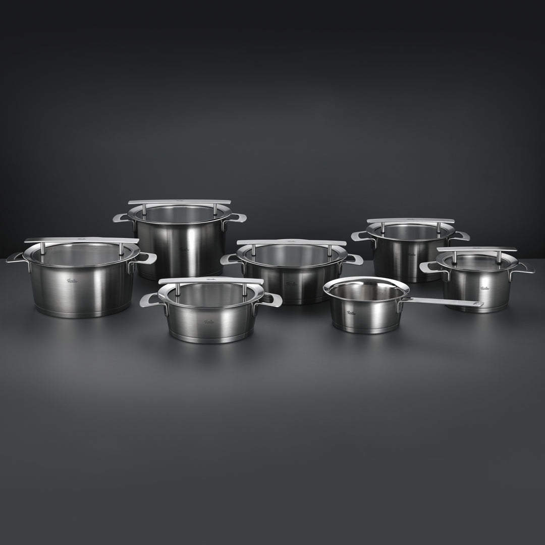 Sieben Fissler Edelstahltöpfe und -kasserollen mit Deckeln, in Deutschland in Präzisionsarbeit hergestellt, elegant angeordnet auf dunklem Hintergrund.