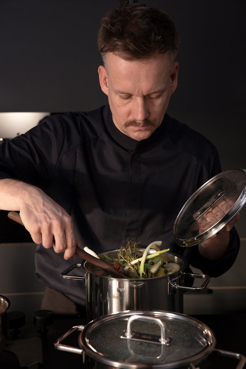 Ein Mann kocht mit dem Fissler Viseo® Pro Kochtopf, hält den Deckel und rührt Gemüse - Präzision und Qualität Made in Germany.