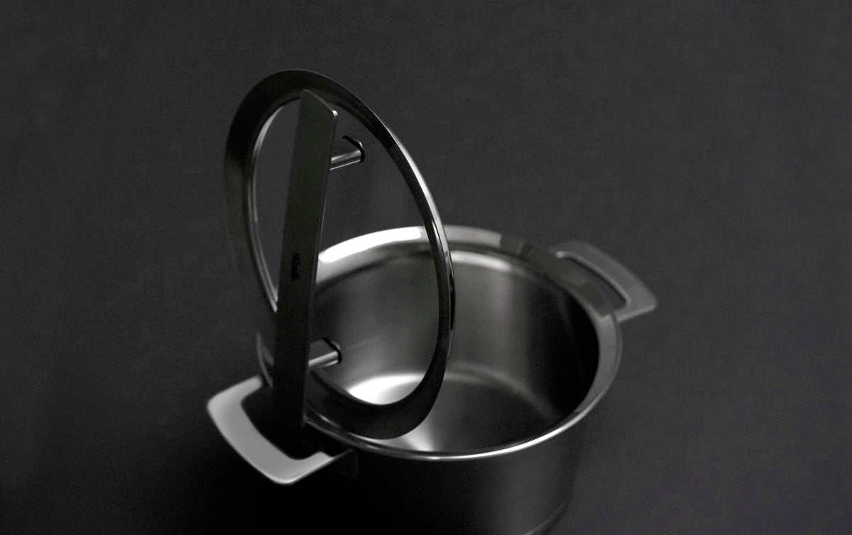 Ein 24 cm großer Glasdeckel aus der Fissler Phi Collection® auf einem 24 cm großen Edelstahltopf, der teilweise geöffnet ist, vor einem dunklen Hintergrund.