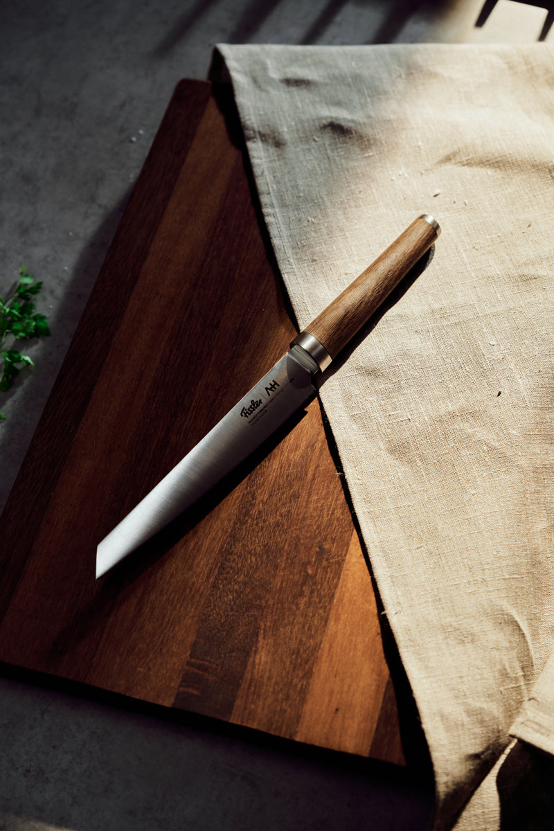 Das Fissler PrimeCut 18cm Fleischmesser mit Holzgriff zeigt deutsche Präzision auf einem dunklen Brett, das Sonnenlicht unterstreicht die Qualität.