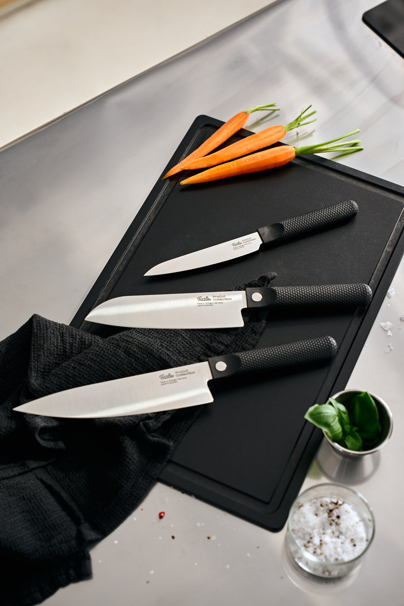 Fissler ProCut 3-teiliges Messerset - deutsches Präzisionsdesign - auf schwarzem Brett mit Karotten, Basilikum und grobem Salz, modernes Ambiente.