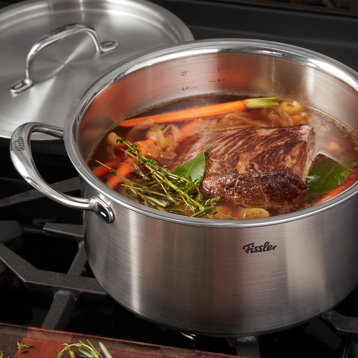 Ein Fissler M5 Pro-Ply® Kochtopf aus recyceltem Edelstahl mit passendem Metalldeckel steht auf dem Herd. Im Topf köcheln Brühe, frisches Gemüse, Kräuter und ein großzügiges Stück gebratenes Fleisch – perfekt für anspruchsvolles Kochen. Der Topf vereint deutsche Präzision und langlebige Qualität, ist induktionsgeeignet sowie spülmaschinenfest. Der hochwertige Metalldeckel ergänzt das zeitlose Design und liegt griffbereit daneben.