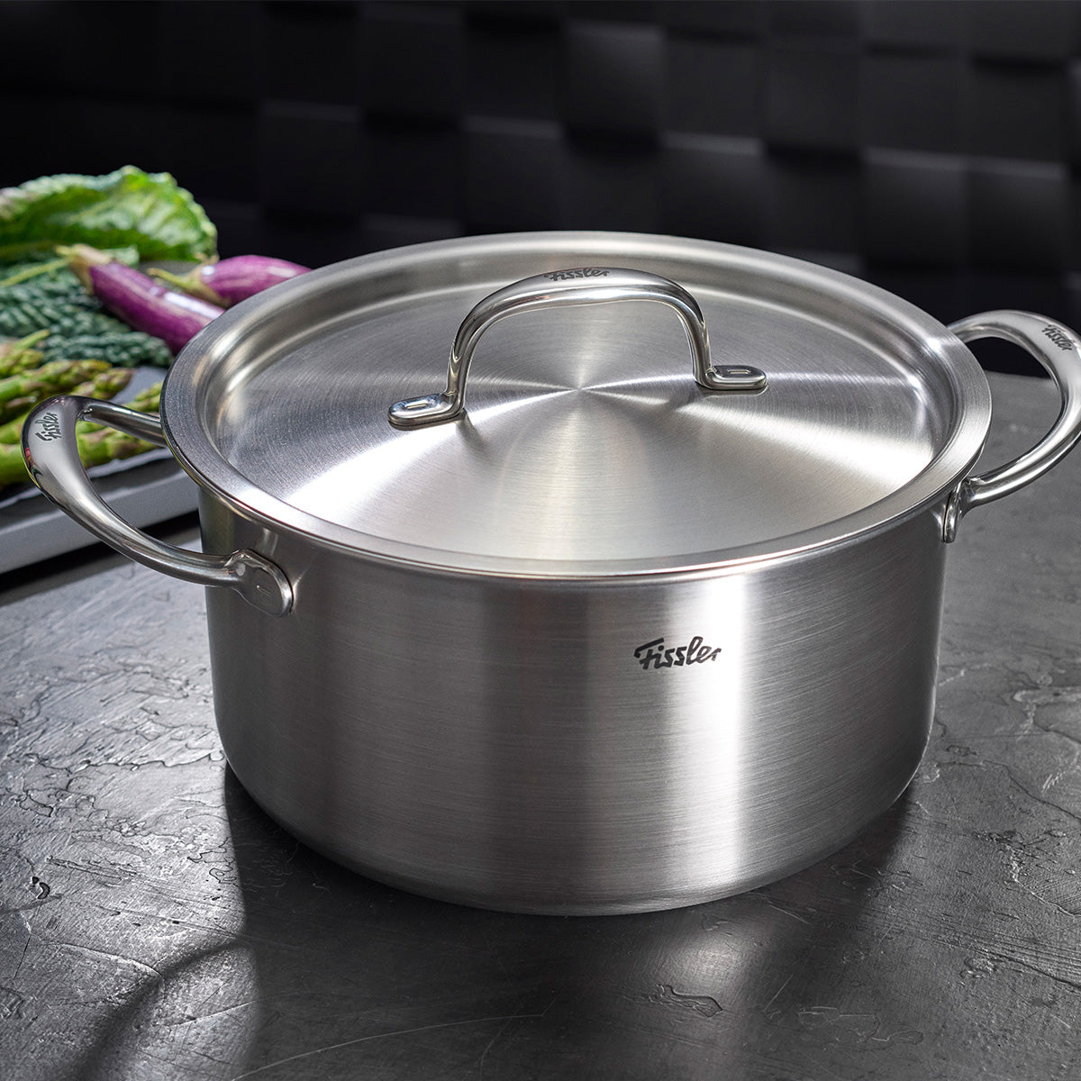 Fissler M5 Pro-Ply Cooking Pot with Metal Lid made from recycled stainless steel, modern and durable, on a dark kitchen countertop.