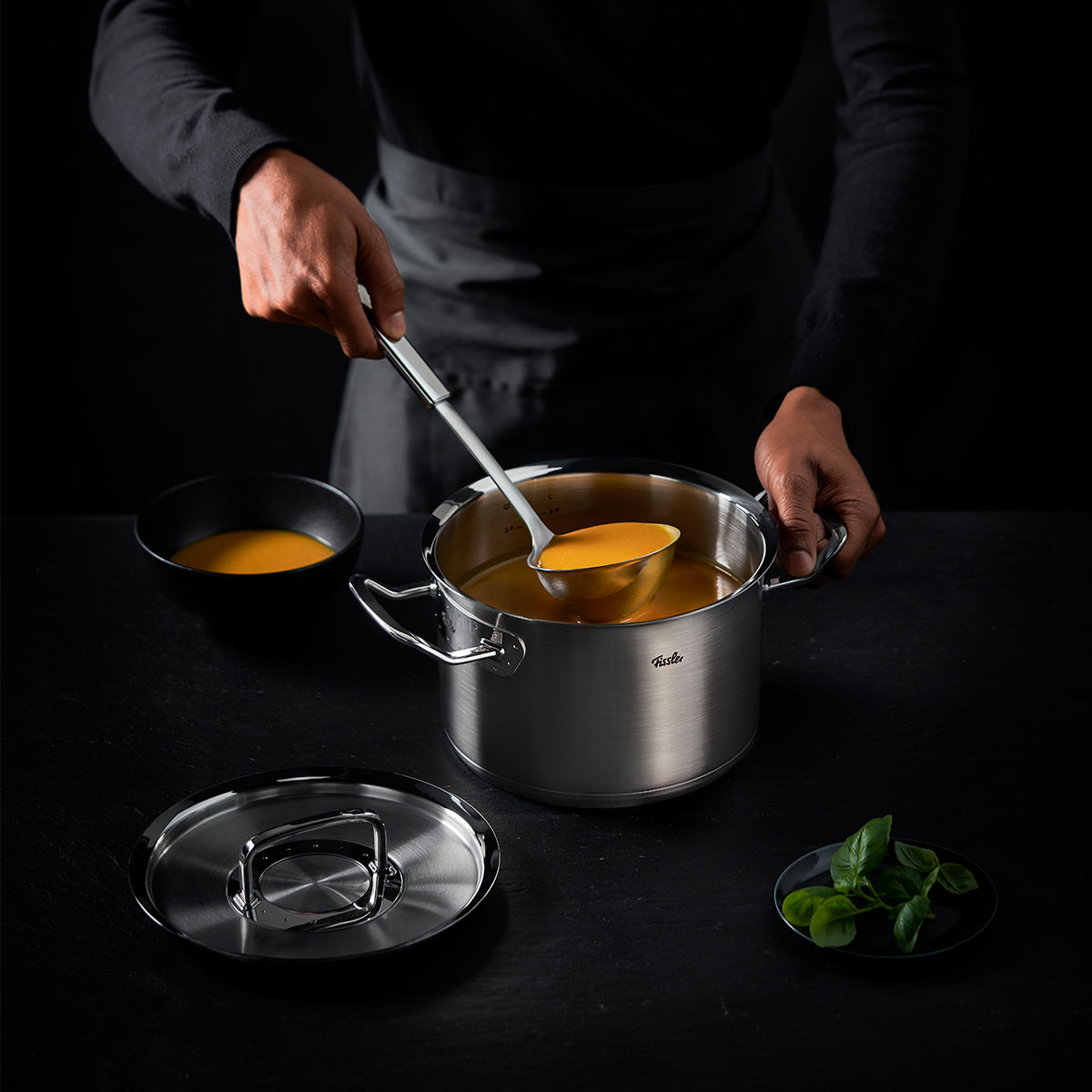 Eine Person löffelt Suppe mit der Fissler Original-Profi Collection® Suppenkelle aus einem hochwertigen Fissler-Topf, der deutsche Präzision ausstrahlt.
