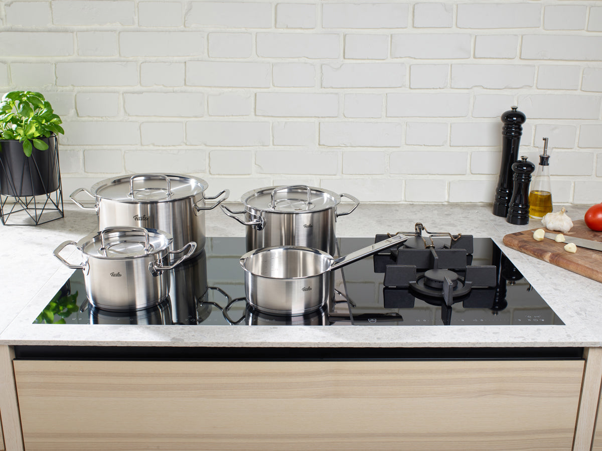 Four pots from the Fissler Original-Profi Collection® with metal lids on an elegant glass stovetop, showcasing German precision and timeless design.