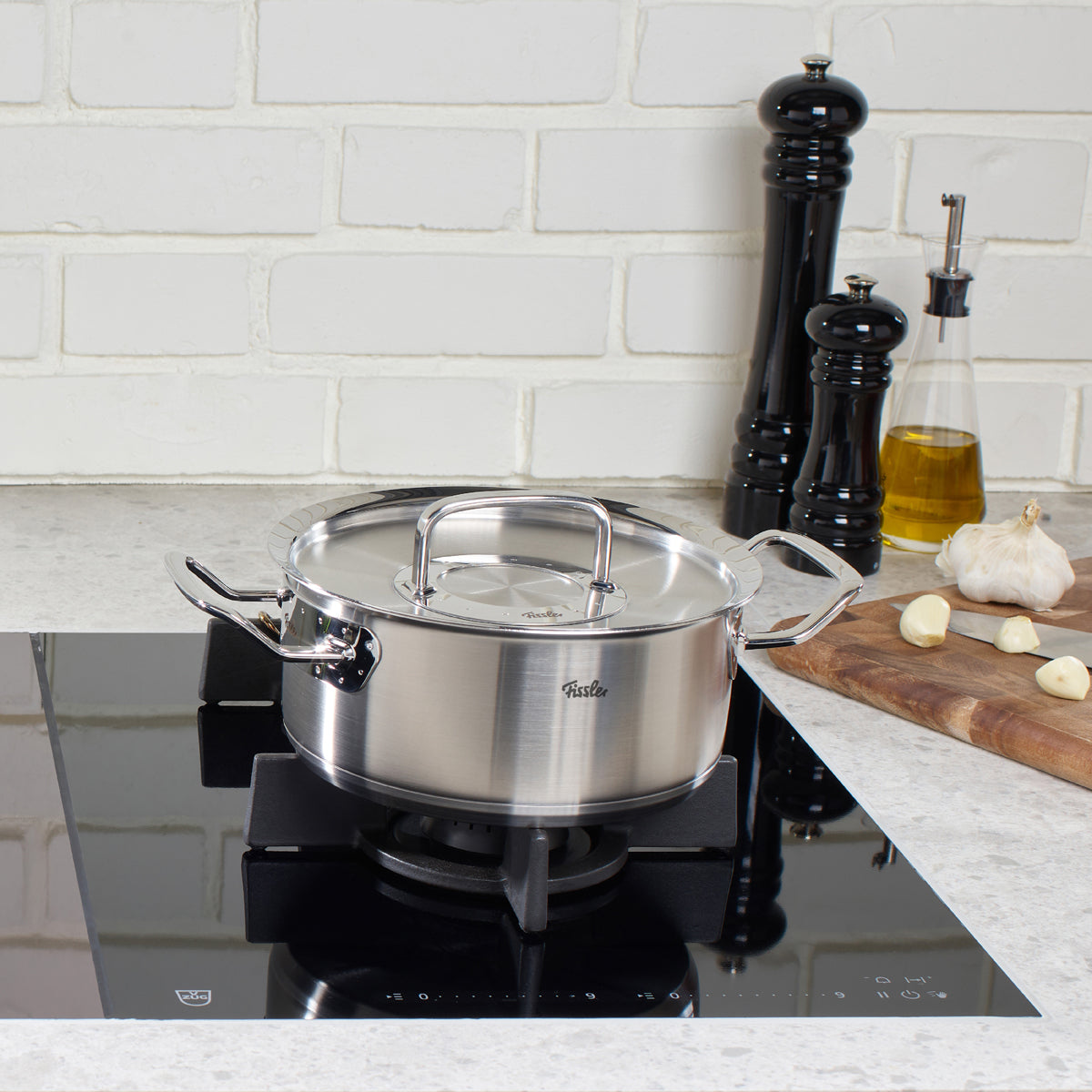 Original-Profi Collection® Bratentopf von Fissler auf Gasherd, mit Metalldeckel. Induktionsgeeignet. Modernes Küchenzubehör im Hintergrund.