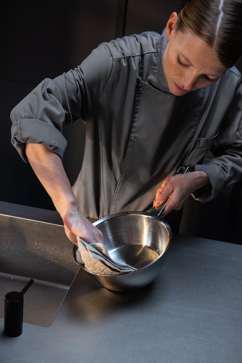A chef in grey polishes a Fissler Original-Profi Collection® 20cm sauté pan, showcasing German precision and timeless design.