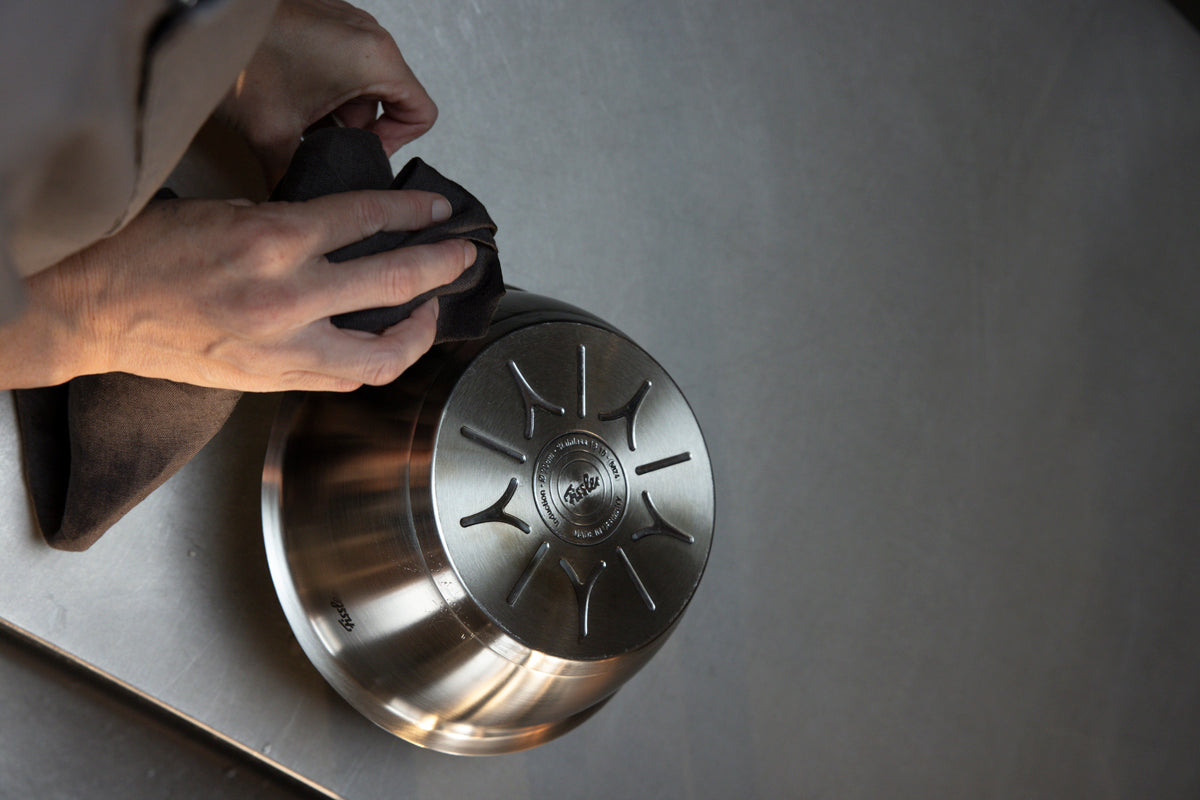 The Fissler Original-Profi Collection® 20 cm sauté pan, made in Germany, is polished upside down on a smooth metal surface.