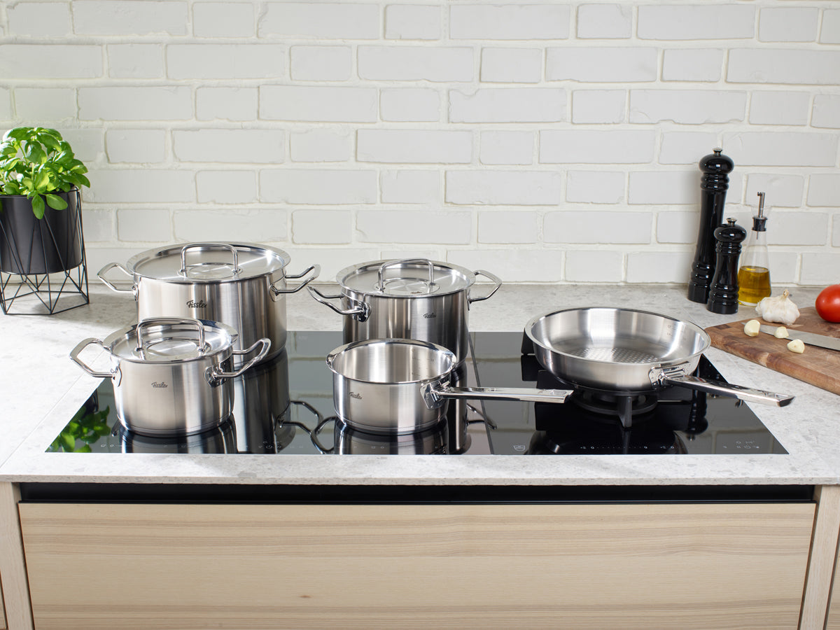Fissler Original-Profi Collection® 5-Piece Set: four stainless steel pots & pans, premium 18/10 steel, for induction cooktops, fresh herbs nearby.