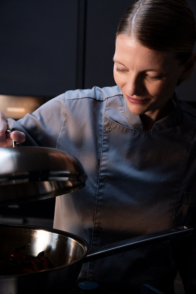 A chef lifts the lid of a Fissler Original-Profi Collection® wok 32cm, showcasing precision and timeless design in a modern kitchen.