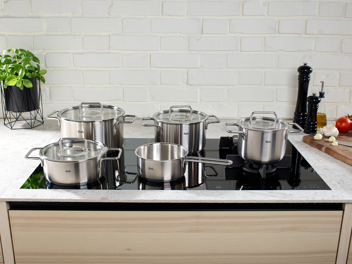 The 5-piece Fissler Pure Collection® Cookware Set shines on a black cooktop in a stylish kitchen, highlighting German precision and design.