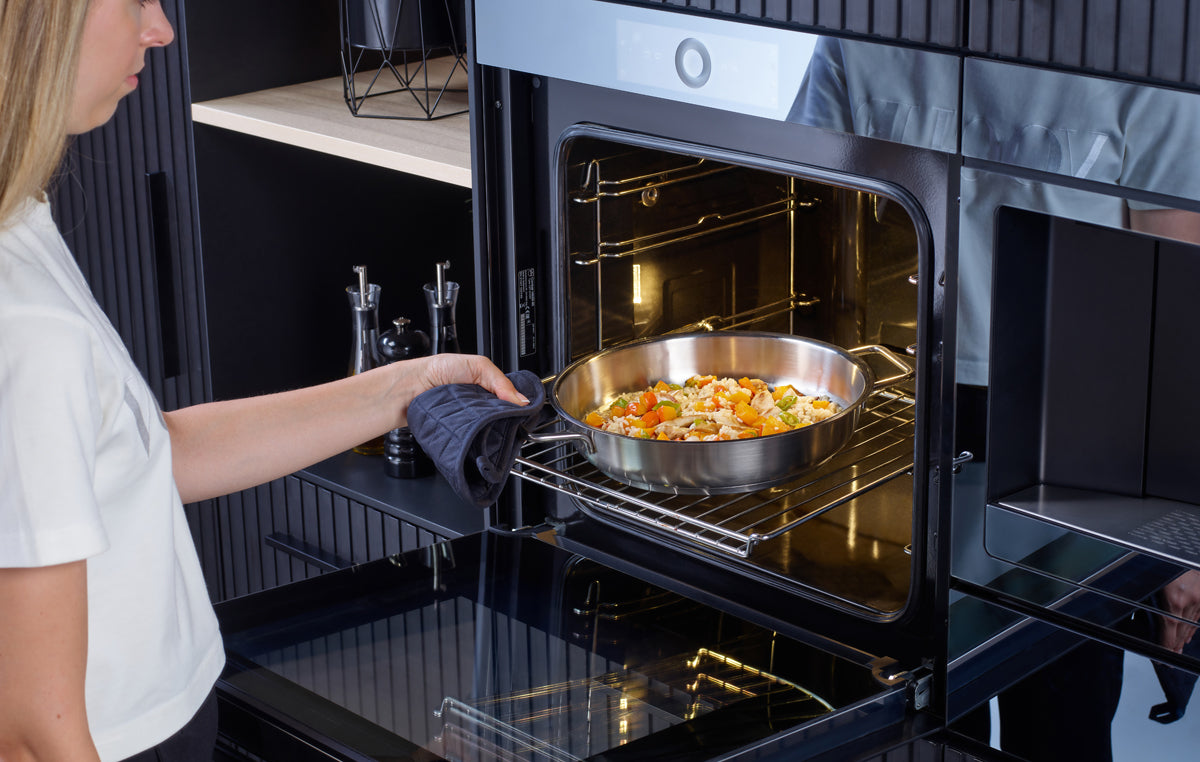 Eine Person schiebt eine Fissler Pure Servierpfanne mit Gemüse in den Ofen; zeitlose deutsche Qualität trifft auf moderne Küchenpräzision.