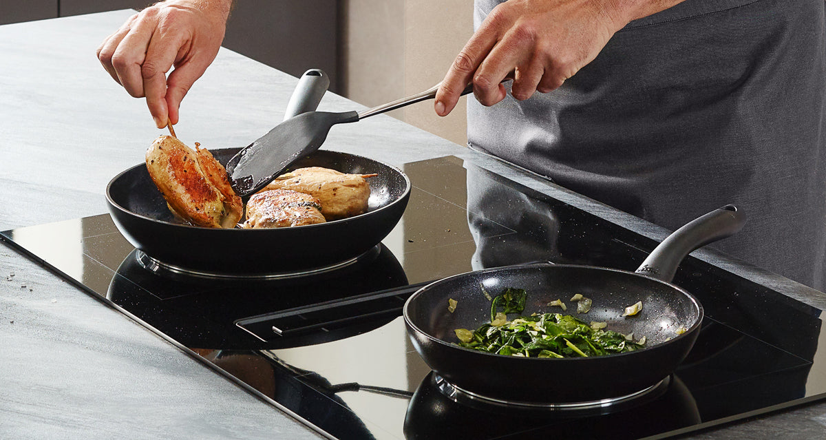 Die Hähnchenbrust wird in einer Fissler Essential®-Pfanne mit einem Edelstahlspatel angebraten, während das Gemüse in einer weiteren Präzisionspfanne "Made in Germany" sautiert wird.