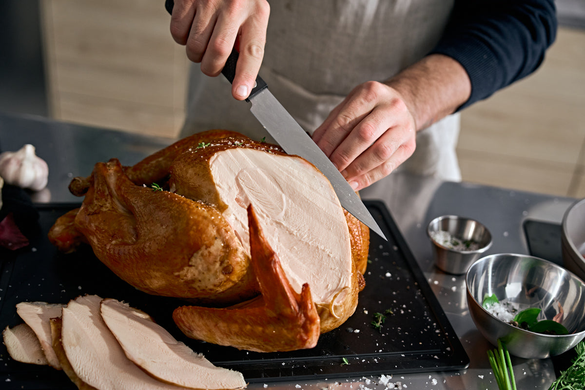A person is slicing turkey breast with the Fissler ProCut 18cm meat knife on an elegant black cutting board, showcasing precision and design.