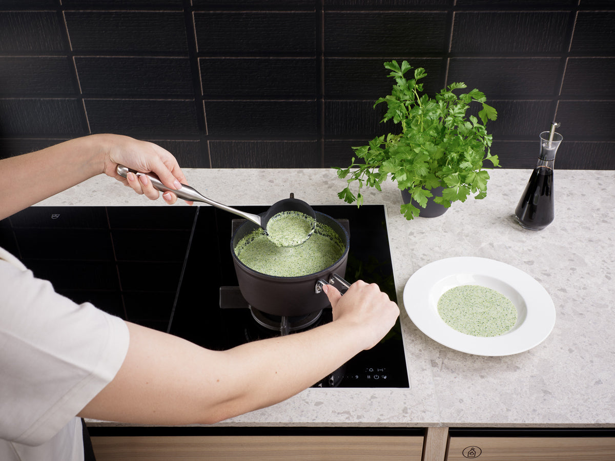 Die grüne Suppe wird aus einem Adamant®-Topfset von Fissler - deutsches Präzisionskochgeschirr seit 1845 - in einer Schüssel serviert, daneben liegen Petersilie und Soße.