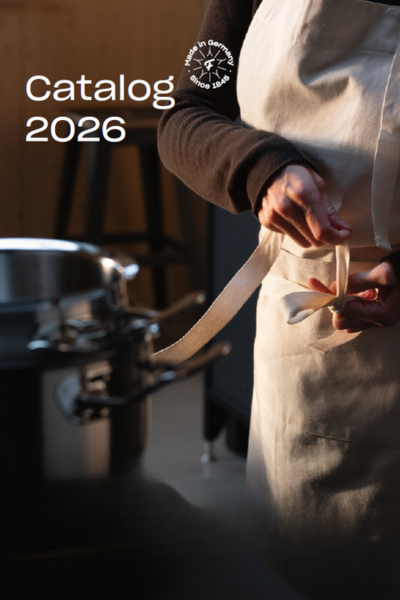 Eine Person in weißer Schürze bindet den Bauchgurt neben einem hochwertigen Fissler-Edelstahltopf. Oben links steht "Katalog 2026".