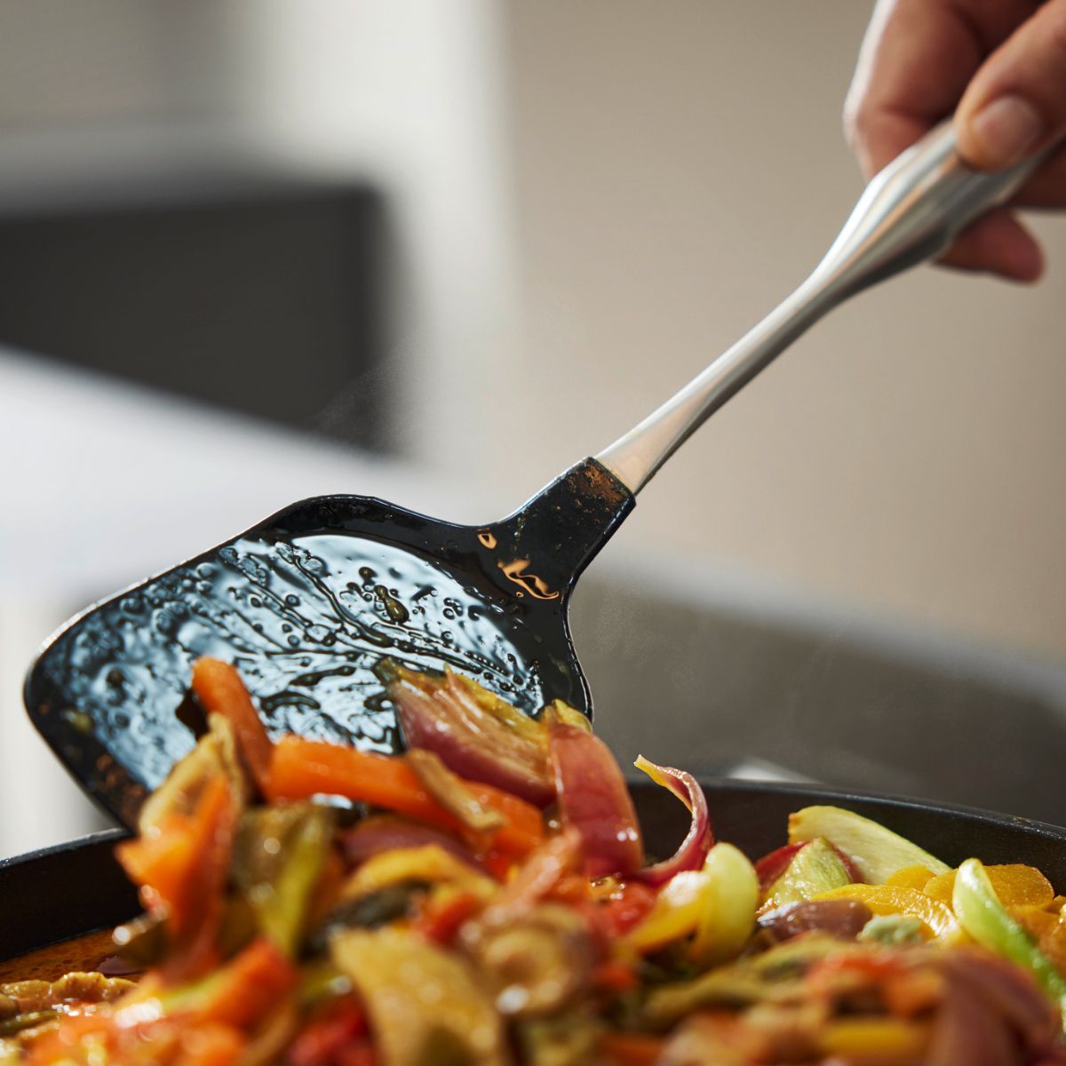 Eine Hand rührt bunte Paprika, Zwiebeln und Pilze in einer Pfanne mit dem Fissler Essential® Wokwender mit Silikon - Präzision in Aktion.