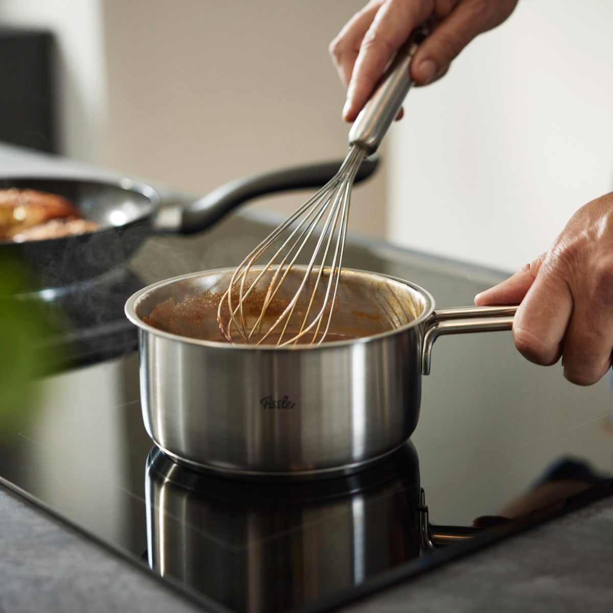 Mit deutscher Präzision rührt ein Koch in einem Fissler-Edelstahltopf mit dem Fissler Essential® Schneebesen 25 cm.