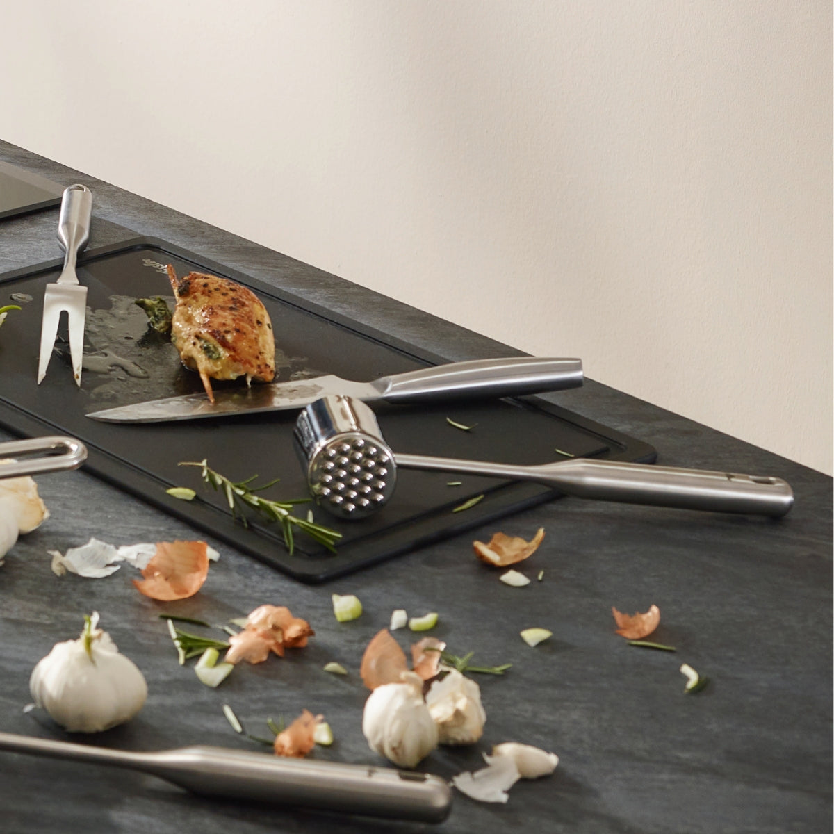 Der Fissler Essential® Fleischklopfer - Präzisionsarbeit aus Deutschland - steht neben Knoblauch und Rosmarin auf einer modernen Küchenzeile.
