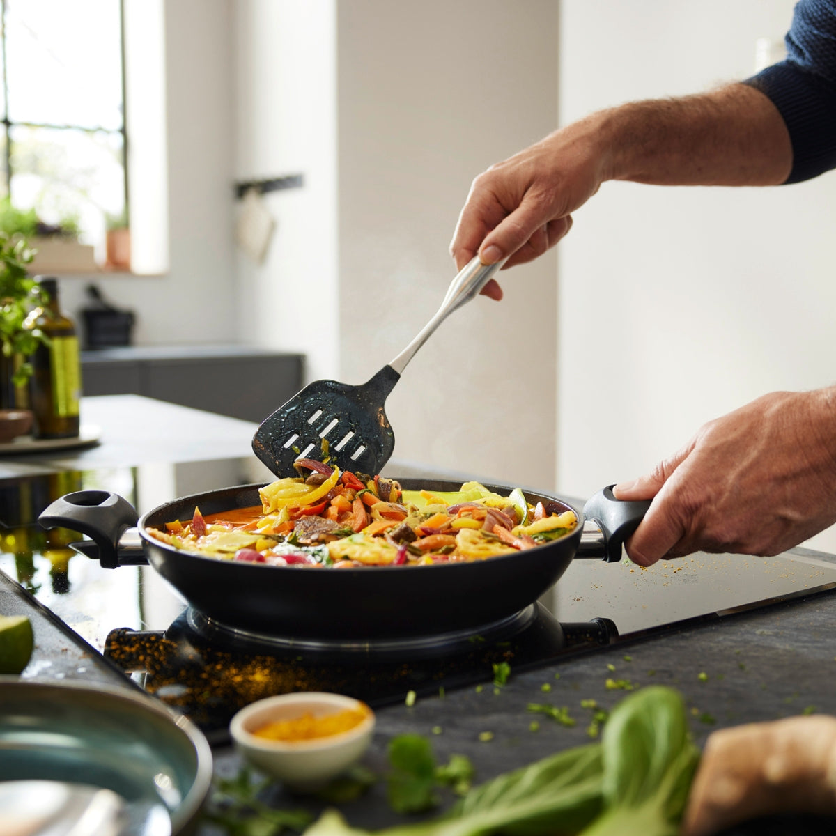 A vibrant vegetable pan dish in a Fissler Essential® Serving Pan 28 cm with herbs and spices, in a modern German kitchen.