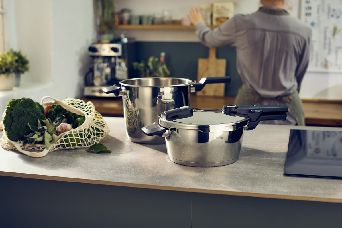 Fissler Vitaquick® Elemental 3-tlg. Schnellkochtopf-Set auf der Theke, Edelstahl-Design neben Frischwaren.