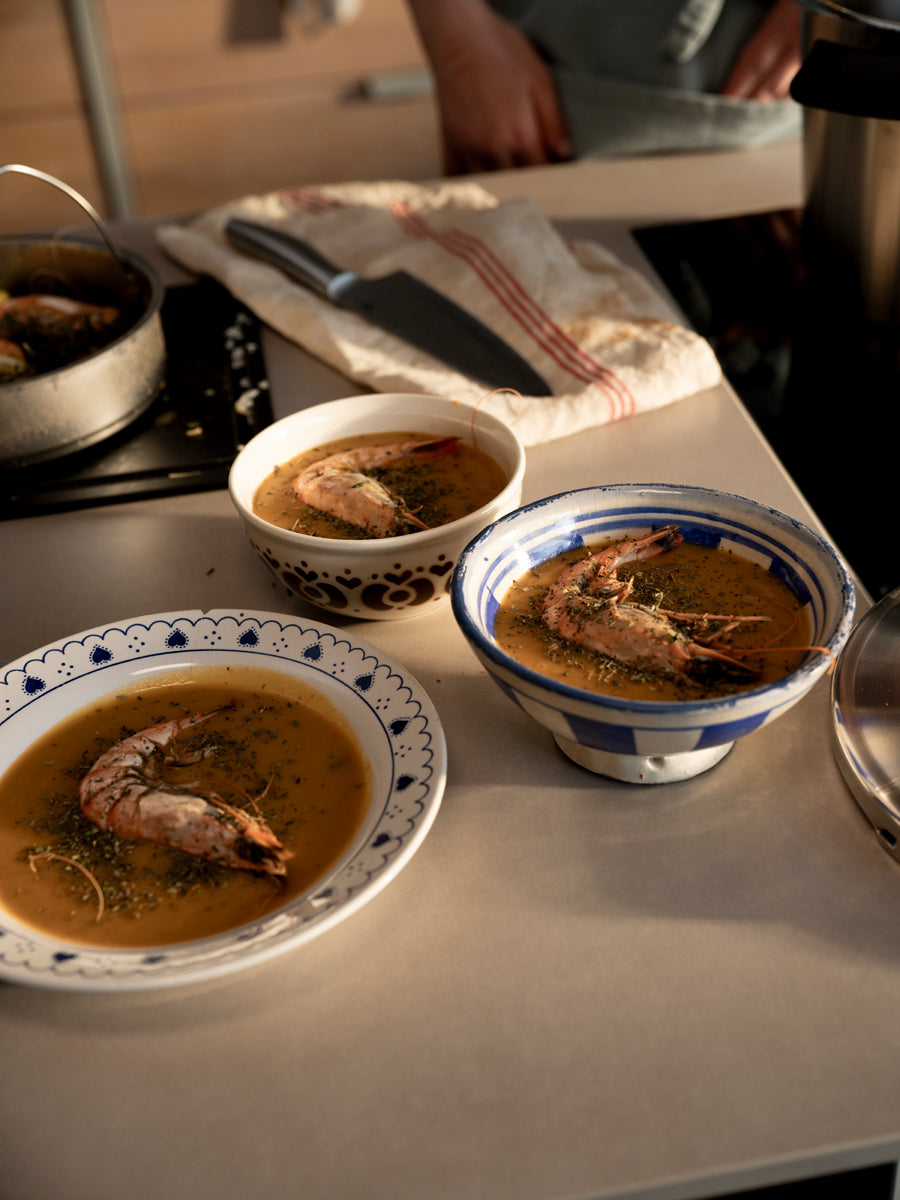 Three bowls of crab soup on a kitchen counter with a Fissler pot and knife, radiating German quality and timeless design. Warm lighting.