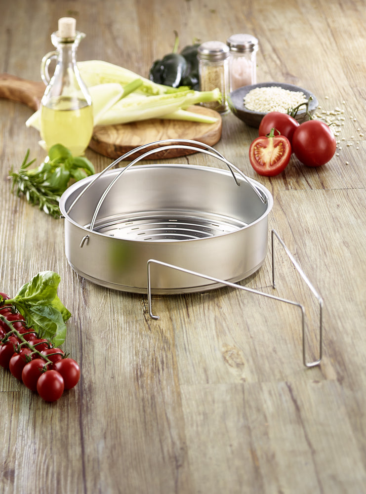 Fissler Edelstahl-Dämpfeinsatz mit Dreibein auf Holzoberfläche, umgeben von frischem Gemüse und Kräutern für gesundes Kochen.