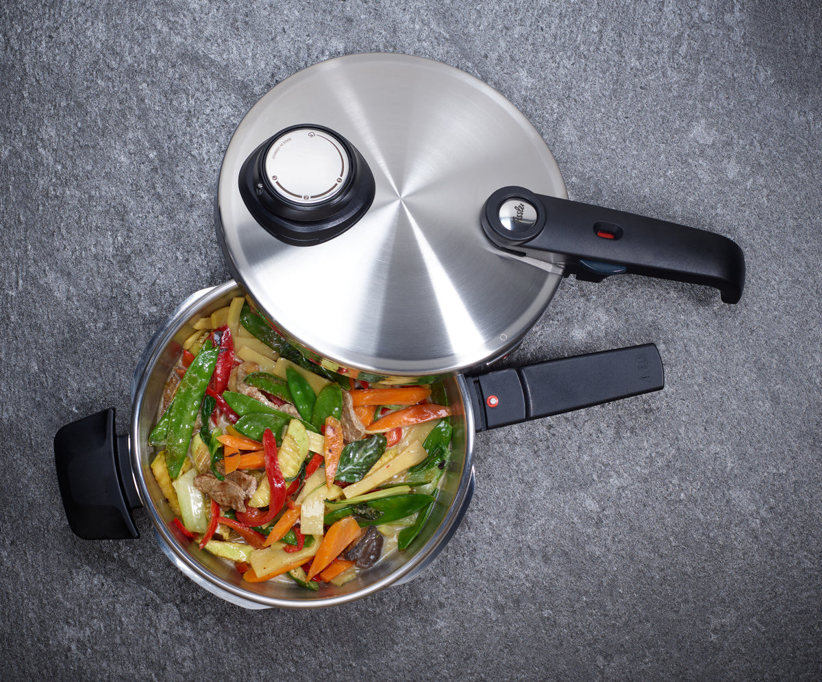 Fissler Vitavit® Premium stainless steel pressure cooker with cooked vegetables and beef strips on a gray surface.