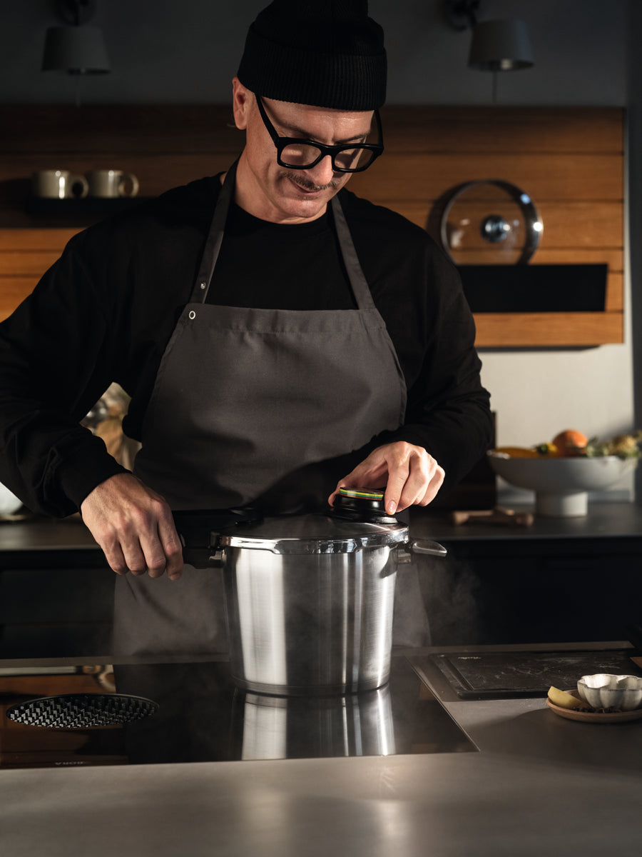 Ein Mann verstellt den Deckel eines Fissler Vitavit® Premium Schnellkochtopfes auf einem Induktionskochfeld in einer eleganten, modernen Küche.