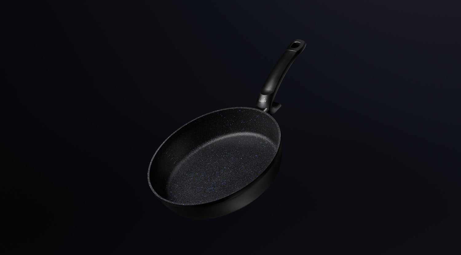 Eine schwarze, antihaftbeschichtete Bratpfanne von Fissler mit einem ergonomischen, langen Griff, der auf einem dunklen Hintergrund mit Farbverlauf angebracht ist, zeugt von deutscher Präzision.