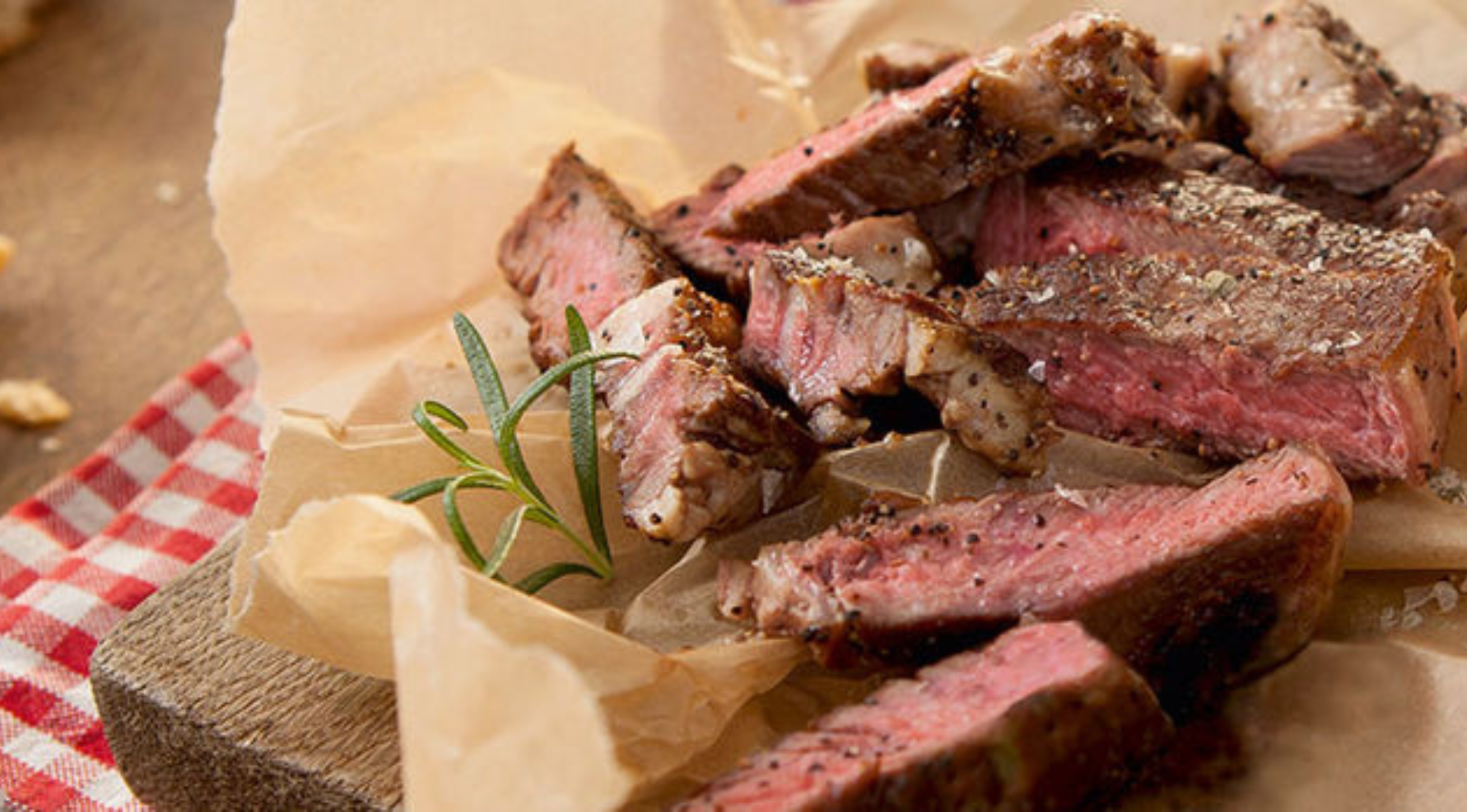 Medium-rare Steak mit Rosmarin auf Pergament, das die Präzision des Fissler-Kochgeschirrs auf einem Holzbrett neben einem karierten Tuch präsentiert.